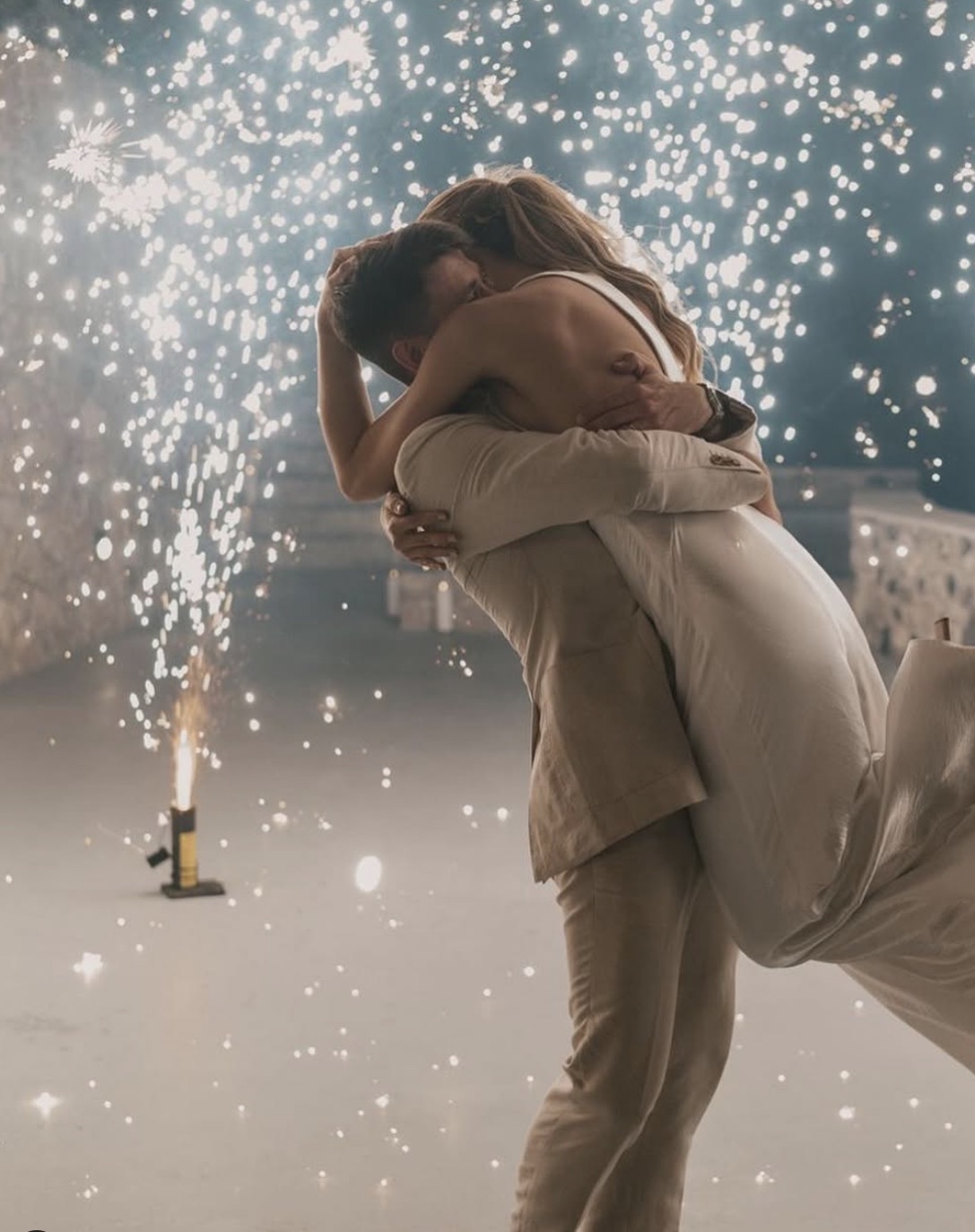 A couple lifted in an embrace with a ground fountain burning beside them