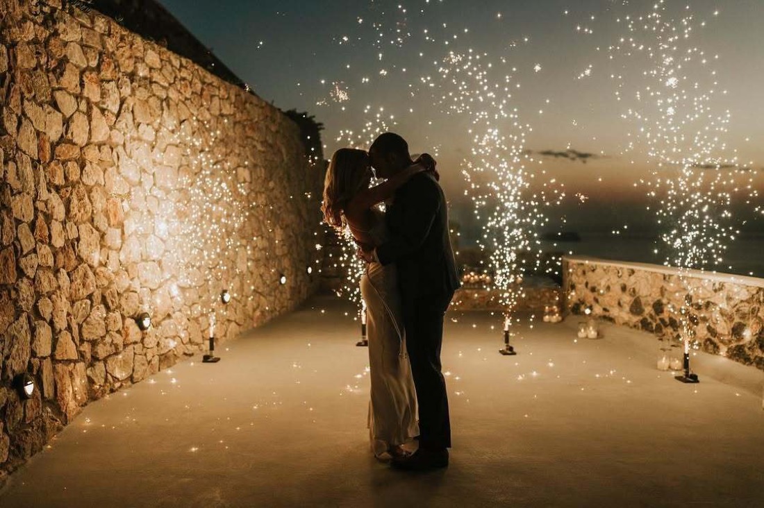 A couple on a stone terrace at dusk with ground fireworks rising